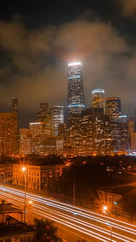 Vertical night timelapse of skyline lighting up with car light trails under cloudy dusk