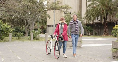 Mature couple strolling through city plaza pushing road bike during cool overcast day