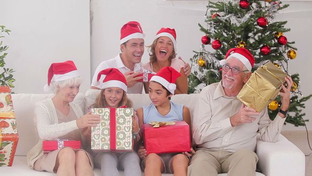 Festive holiday atmosphere with diverse family exchanging Christmas presents in cozy living room. Grandparents, parents, and children gathered happily while wearing Santa hats. Ideal for depicting joyful holiday celebrations, family gatherings, and Christmas traditions.