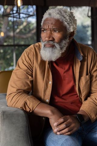 Senior african american man sitting on sofa leaning forward thoughtful in sunlit room