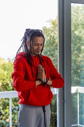 African american man practicing balcony meditation in red hoodie and gray sweatpants