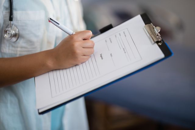 Midsection of female doctor writing on clipboard in hospital ward. Ideal for use in healthcare, medical, and hospital-related content. Can be used in articles, blogs, and promotional materials focusing on patient care, medical documentation, and healthcare professionals.