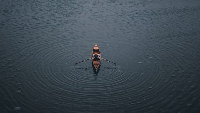 Rowing alone on calm lake creating concentric ripples minimalist moody overcast composition