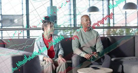 Discussing market charts on sofa with candlestick graphs overlay for finance collaboration