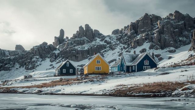Colorful coastal cottages sitting on snowy shoreline beneath rocky mountain cliffs