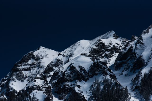 High-resolution image of snow-covered mountain peaks contrasting with a deep blue sky. Ideal for outdoor adventure themes, travel brochures, websites about natural beauty, winter sports promotions, and magazine covers. Perfect for bringing the serenity and grandeur of nature into environmental campaigns and digital or print backgrounds.