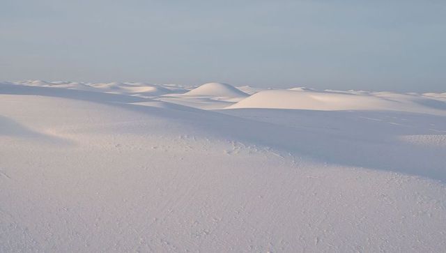 Endless white dune field with rounded crests and rippled texture under pale sky