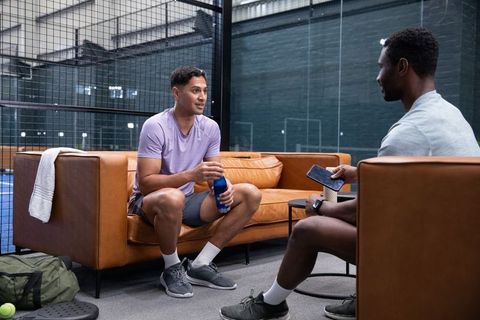 Two men chatting on cognac leather sofa in sports court lounge holding water bottle