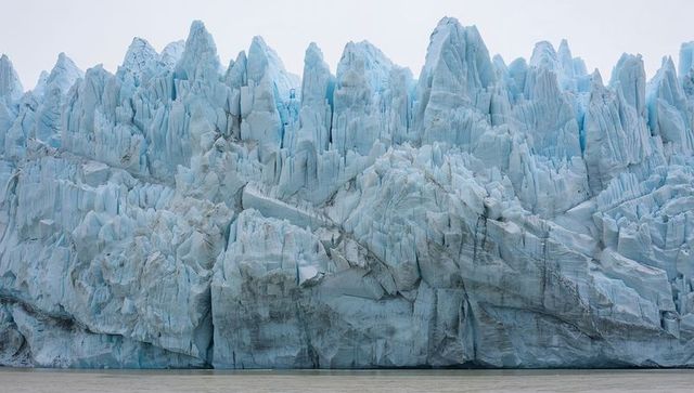 Towering glacier front revealing jagged seracs and deep crevasses at calm fjord