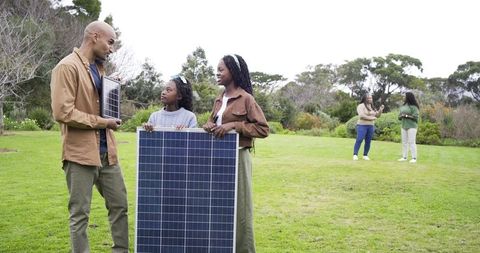 Multigenerational family holding solar panels in park promoting renewable energy education