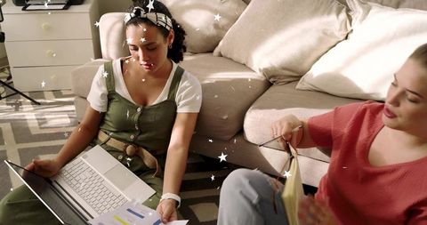 Two Women Collaborating on Project in Living Room with Laptop and Papers