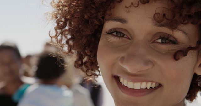 Cheerful woman with curly hair enjoying a sunny day outside. Perfect for content about happiness, outdoor activities, human connections, and lifestyle themes.