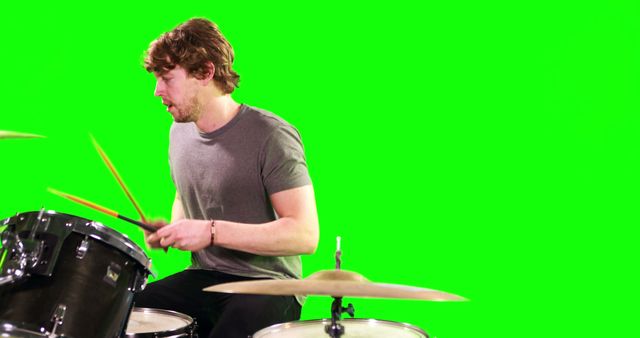 Young man enthusiastically playing drum set against green screen background. Ideal for projects where customizable backgrounds are needed, music-related themes, promoting musical instruments or bands, or educational materials on how to play the drums.