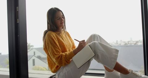Woman enjoying quiet journaling near window in cozy sweater