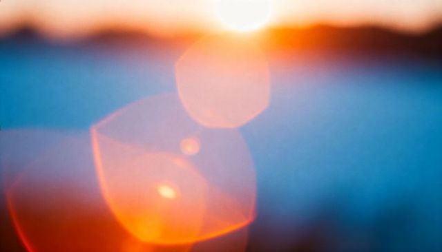 Sunset lens flare with hexagonal bokeh and warm orbs over cool blue horizon abstract glow