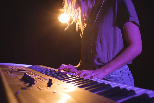 This image captures a female musician playing the piano on stage under a spotlight, creating a dynamic and engaging atmosphere. Ideal for use in articles or promotions related to live music events, concerts, music education, or nightlife entertainment. It can also be used in marketing materials for music venues, piano lessons, or music festivals.