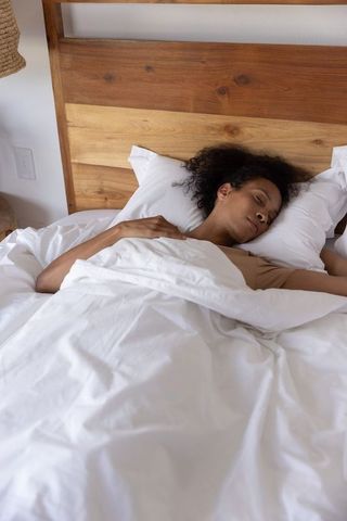 African american woman sleeping under white duvet on wooden headboard in cozy bedroom