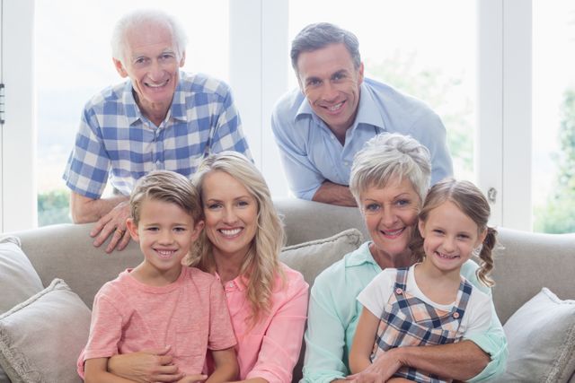Multi-generational family sitting on a sofa in a bright living room, smiling and enjoying time together. Ideal for use in family-oriented advertisements, articles on family bonding, or promotional materials for home and lifestyle products.