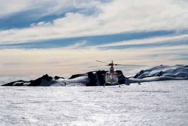 Helicopter is landing on a vast, snowy mountain landscape with a breathtaking backdrop of sky and rugged terrain. This could be used for travel blogs, adventure tourism advertisements, or content related to remote expeditions and outdoor activities.