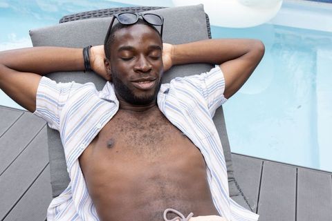 African american man relaxing on poolside lounge chair in striped shirt and sunglasses
