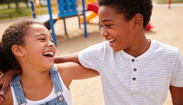 Laughing siblings hugging at sunny playground with colorful slide and climber