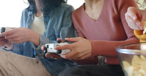 Friends playing couch multiplayer with wireless controller and snacks, cozy gaming night