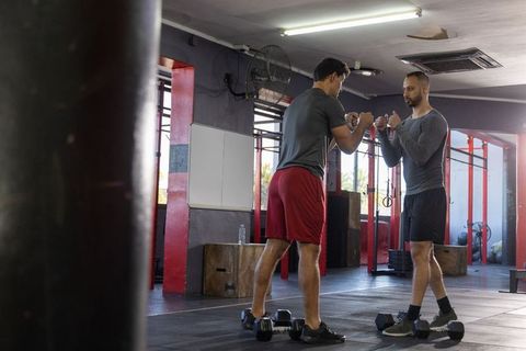 Male trainer coaching trainee in partner strength drill with dumbbells in crossfit gym
