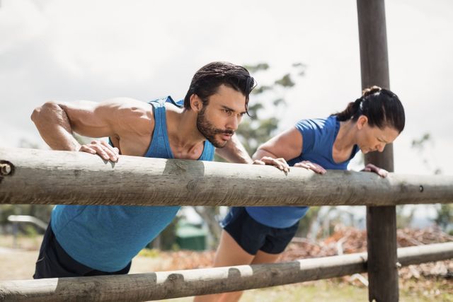 Fit individuals performing pushups on wooden bars in an outdoor boot camp. Ideal for promoting fitness programs, outdoor training sessions, and healthy lifestyle campaigns. Can be used in advertisements for gyms, fitness classes, and sports events.
