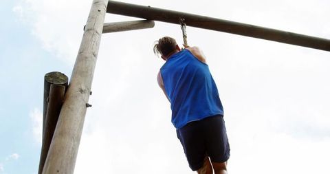 Athlete hanging and gripping ring and chain on wooden rig at outdoor obstacle course training