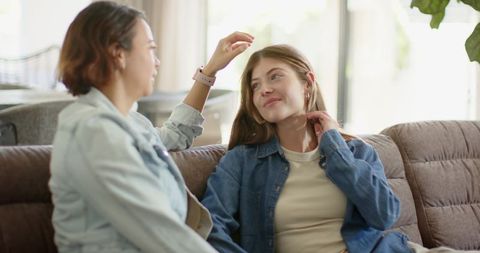Young women chatting on sofa wearing denim, cozy home conversation and friendship