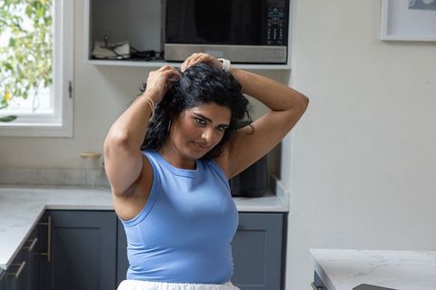 Indian woman adjusting curly hair in modern sunlit kitchen, getting ready at counter