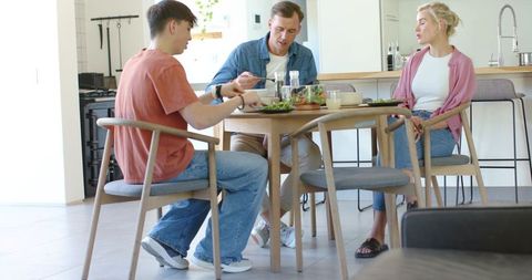 Family sharing healthy salad around round wooden dining table in bright modern kitchen