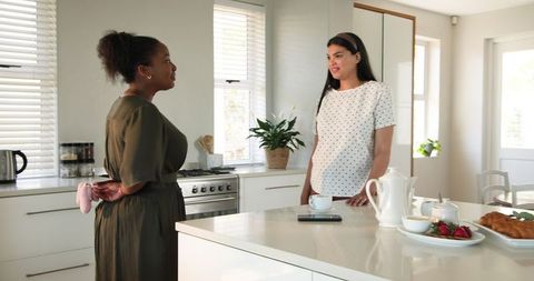 Two women chatting and celebrating pregnancy in bright kitchen