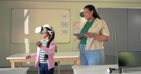 Teacher Guiding Student with VR Headset in Classroom Using Tablet for Interactive Learning