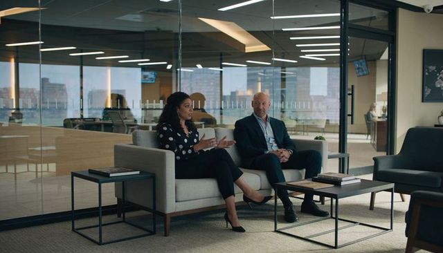 Business discussion in glass office lounge with gesturing woman and attentive executive