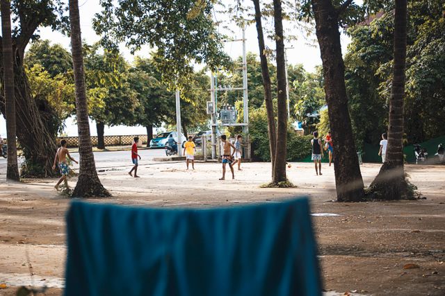 Children enthusiastically playing outdoors amidst lush greenery and large trees. Perfect for depicting scenes of community, childhood joy, outdoor activities, and rural life. Useful for advertising children's products, outdoor gear, lifestyle blogs, and educational programs promoting play and physical activity.
