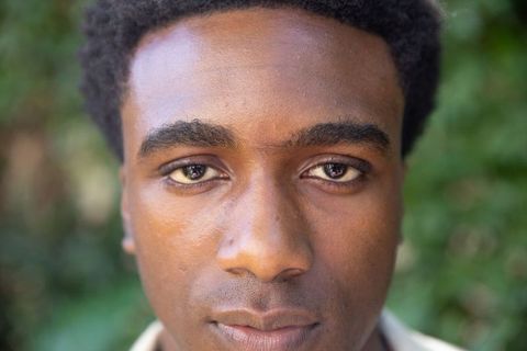 Young man with natural expression in green foliage background outdoors