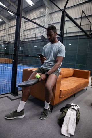 Athletic african american man checking phone on leather couch after padel practice