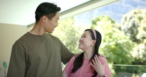 Sunlit couple smiling on balcony embracing modern home life with smartwatch and headband