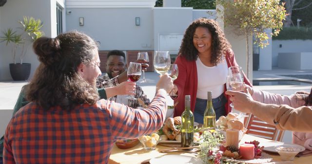 People raising glasses while enjoying a meal outside on a sunny day. Cultural diversity. Great for illustrating social gatherings, friendship, summer fun, and outdoor dining.