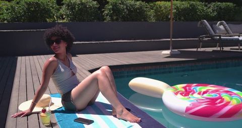 African american woman relaxing poolside on striped towel with cocktail and lollipop float