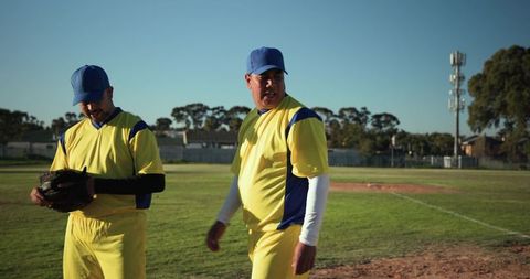 Community baseball teammates standing on sunlit field holding glove wearing yellow uniforms