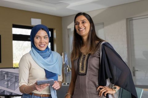 Diverse women reviewing tablet and floor plan in modern office wearing hijab and kurta