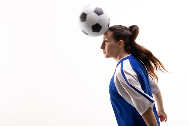 Side view of female caucasian athlete heading soccer ball by copy space on white background. unaltered, sport, competition and game concept.