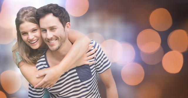 Young woman happily hugging her boyfriend from behind with festive bokeh lighting in the background. Great for advertisements about relationships, romance, outdoor activities, and joyful moments. Can be used for social media posts, articles on love and companionship, or projects centered on happiness and bonding experiences.