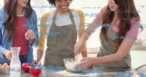 Three friends mixing batter in sunlit kitchen wearing aprons and casual clothing