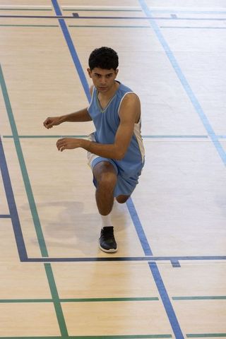 Athlete kneeling defensively on indoor basketball court