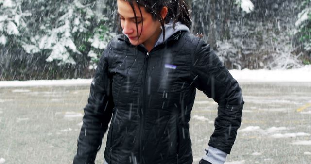 A young woman stands outdoors dressed in a black winter jacket while snow falls heavily around her. This image can be used for promoting winter apparel, depicting outdoor winter activities, or illustrating nature-related content.