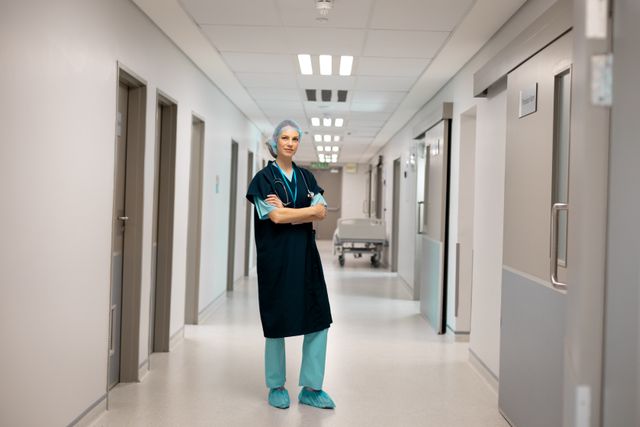 Portrait of smiling caucasian female doctor in scrubs and surgical cap standing in hospital corridor. Medical services, hospital and healthcare concept.