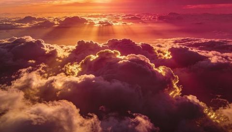 Golden rim-lit clouds radiating sunset rays over expansive aerial horizon